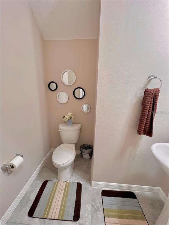 A small bathroom features a toilet, a wall gallery of mirrors, and two striped rugs — 10007 LEYBURN COURT, ORLANDO, FL