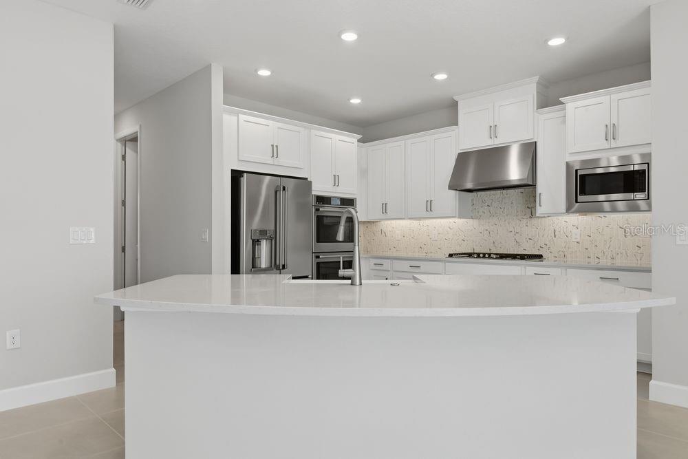 A modern kitchen features white cabinetry, stainless steel appliances, and a marble-patterned tile backsplash — 664 JUNONIA BOULEVARD, NEW SMYRNA BEACH, FL