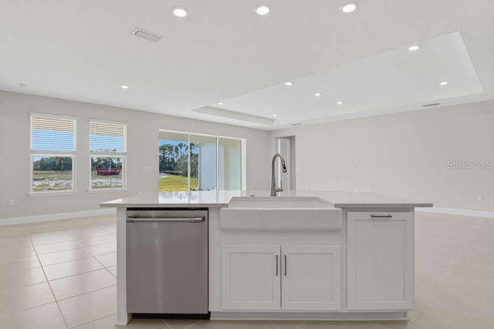 A modern kitchen features white cabinetry, a large island, stainless steel appliances, and quartz countertops — 664 JUNONIA BOULEVARD, NEW SMYRNA BEACH, FL