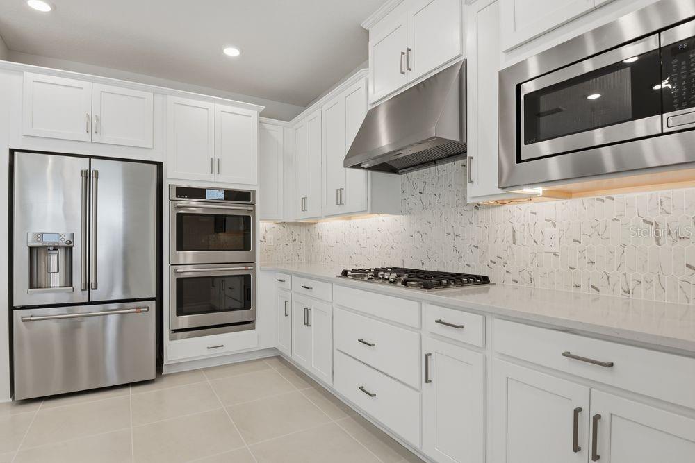 A modern kitchen features white cabinetry, stainless steel appliances, and a large quartz-topped island — 664 JUNONIA BOULEVARD, NEW SMYRNA BEACH, FL
