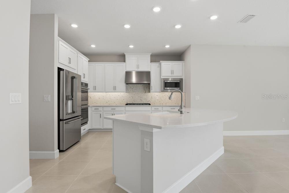 A modern kitchen features white cabinetry, a large quartz island, and stainless steel appliances — 664 JUNONIA BOULEVARD, NEW SMYRNA BEACH, FL
