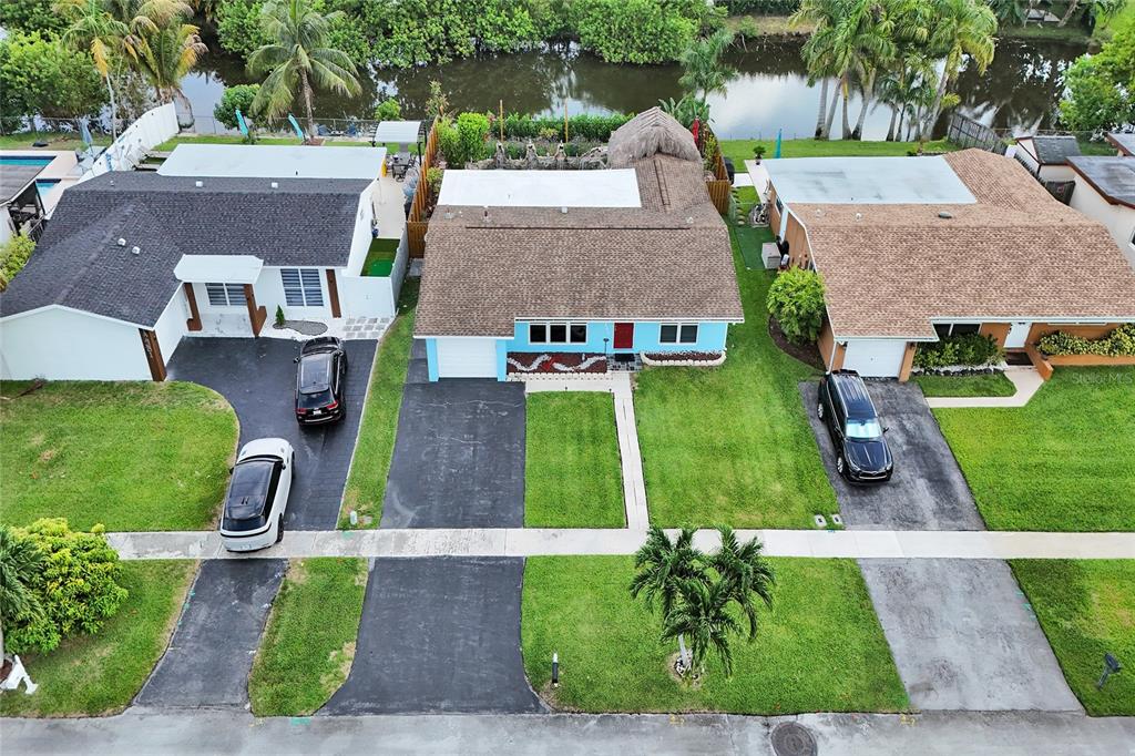 An aerial view shows three suburban houses with driveways, lawns, and a canal in back — 12341 NW 29TH MANOR, SUNRISE, FL