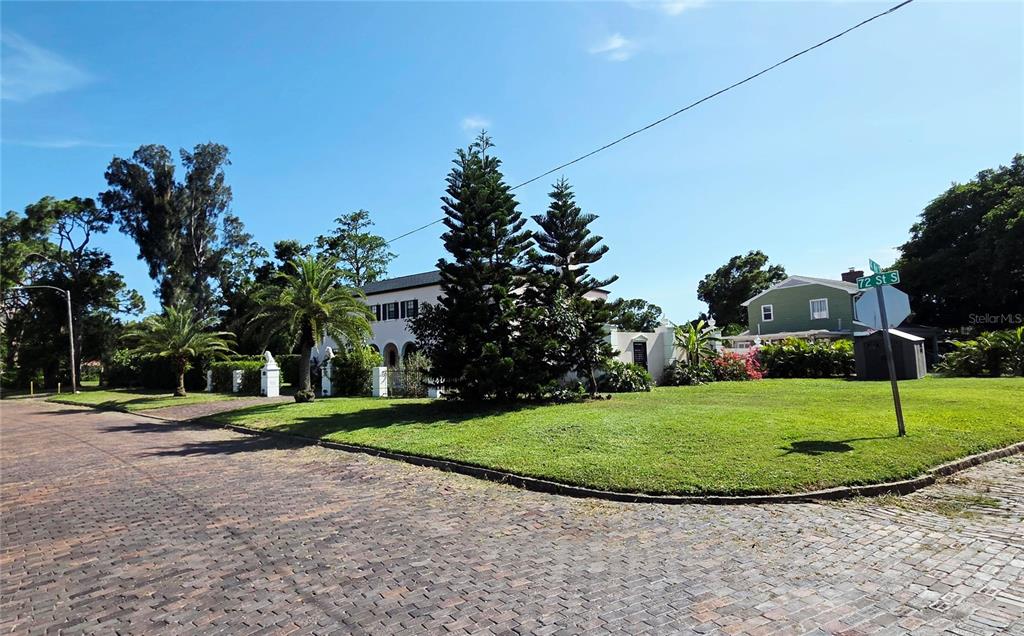 A brick street leads to a two-story house with palm trees and tall pine trees — 411 72ND STREET S, ST PETERSBURG, FL