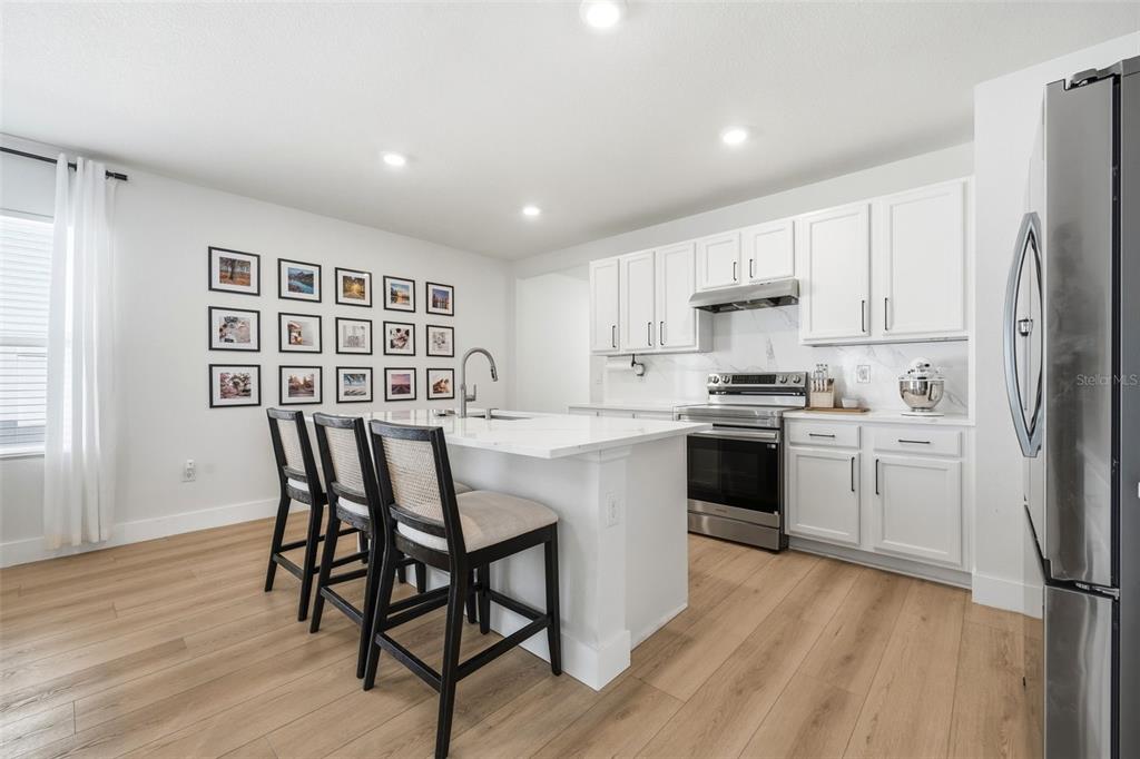 A modern kitchen features white cabinets, a central island with bar seating, and light flooring — 30309 ARMENIA ROAD, LEESBURG, FL