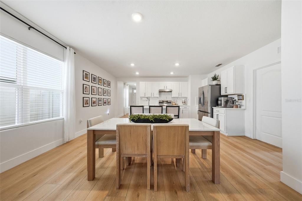 A dining area with a wooden table and chairs opens into a white modern kitchen — 30309 ARMENIA ROAD, LEESBURG, FL