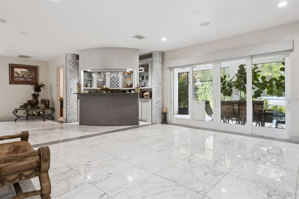 A spacious room features white marble flooring, a curved wet bar, and large glass sliding doors — 8515 BAY LAKE ROAD, GROVELAND, FL