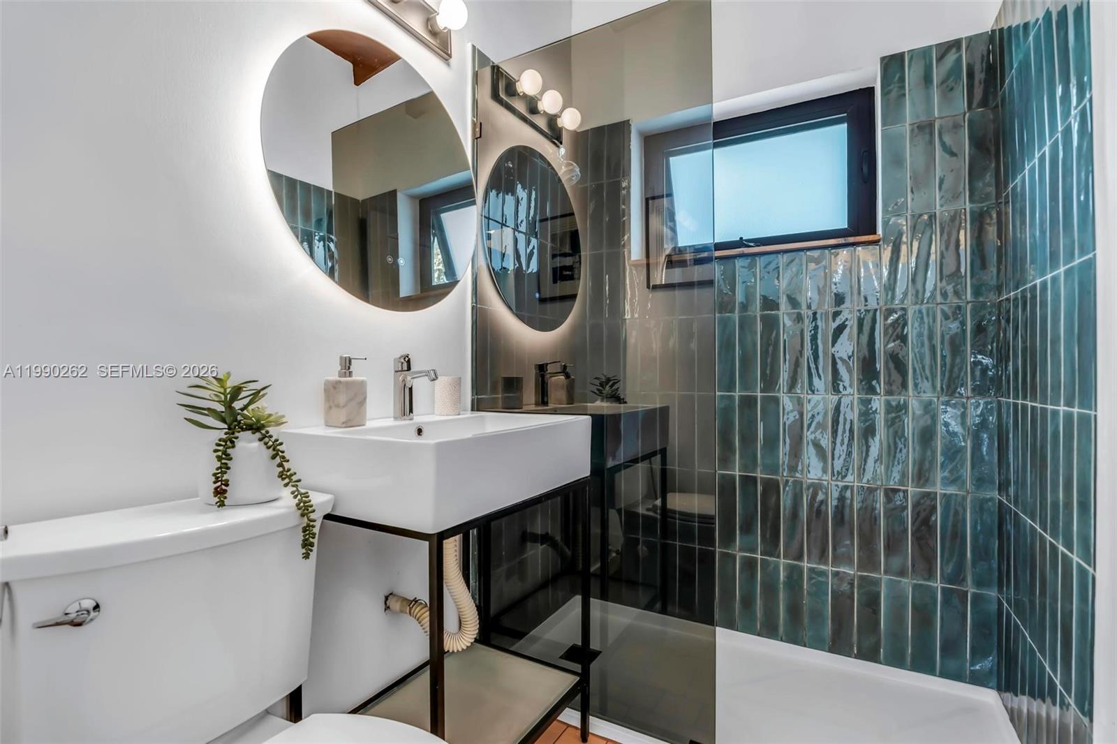 A bathroom features a white vessel sink, a round backlit mirror, and teal wall tiles — 6561 SW 34th St, Miami FL 33155, MIAMI, FL