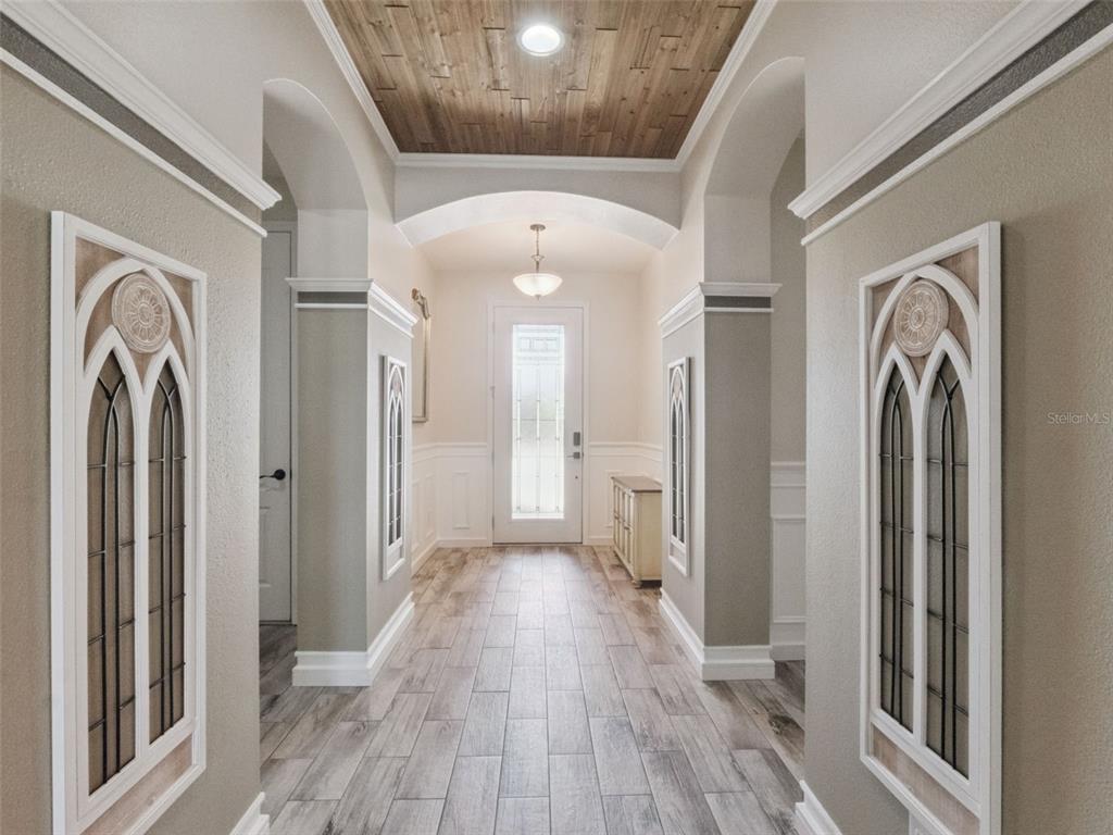 A hallway features arched openings, wood-plank ceiling detail, decorative wall panels, and light wood flooring — 1025 SADIE RIDGE ROAD, CLERMONT, FL