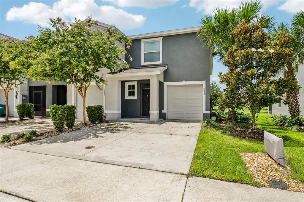 A two-story gray townhouse with a single-car garage, a concrete driveway, and front yard landscaping — 5323 LOBLOLLY LANE, WILDWOOD, FL