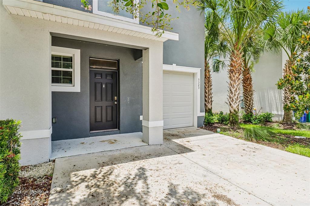 The exterior of a two-story house features a dark front door, a garage, and palm trees — 5323 LOBLOLLY LANE, WILDWOOD, FL