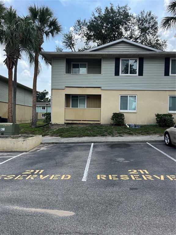 A two-story apartment building exterior features tan stucco, light green siding, and reserved parking spaces — 211 THORN TREE PLACE, BRANDON, FL