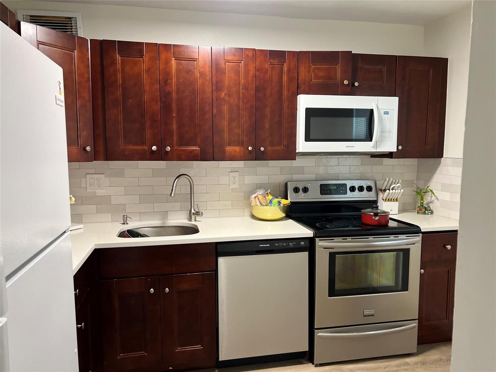 A kitchen featuring dark wood cabinets, stainless steel appliances, a white countertop, and subway tile backsplash — 1061 NW 45th Street # 8, Pompano Beach FL 33064, POMPANO BEACH, FL