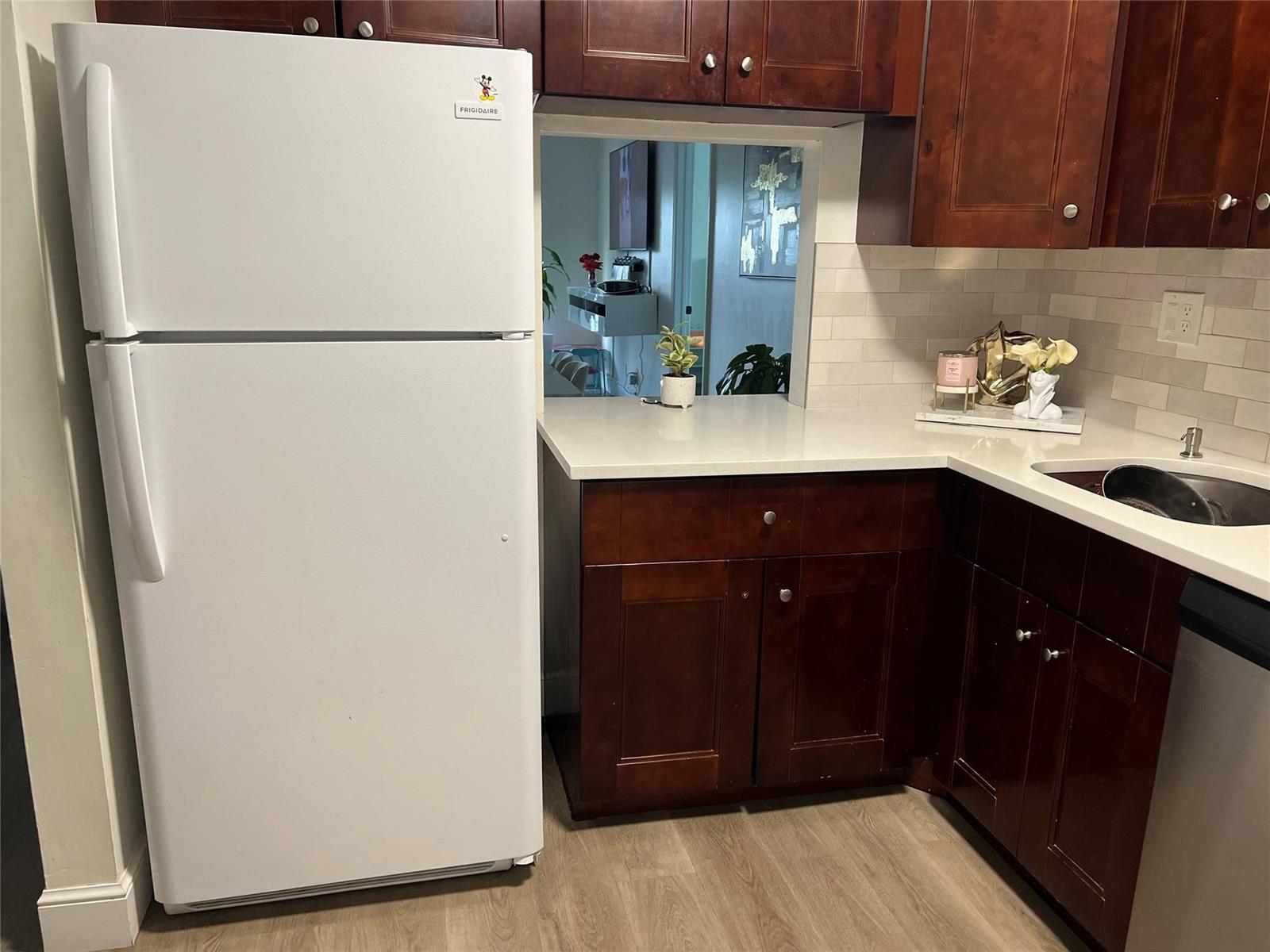 A kitchen features dark wood cabinets, white countertops, a white refrigerator, and a pass-through window — 1061 NW 45th Street # 8, Pompano Beach FL 33064, POMPANO BEACH, FL