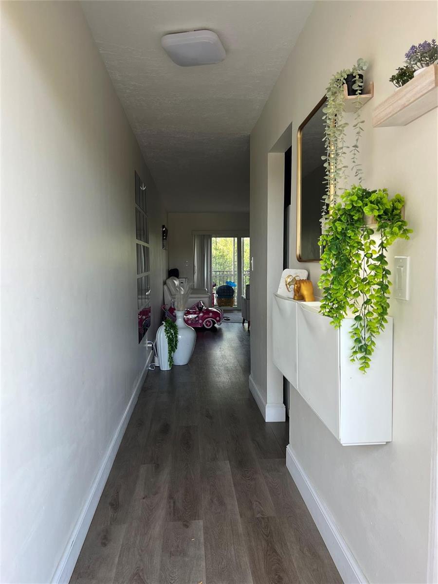 A hallway with wood-look flooring, a wall-mounted shoe cabinet, and a mirror leads to a living area — 1061 NW 45th Street # 8, Pompano Beach FL 33064, POMPANO BEACH, FL