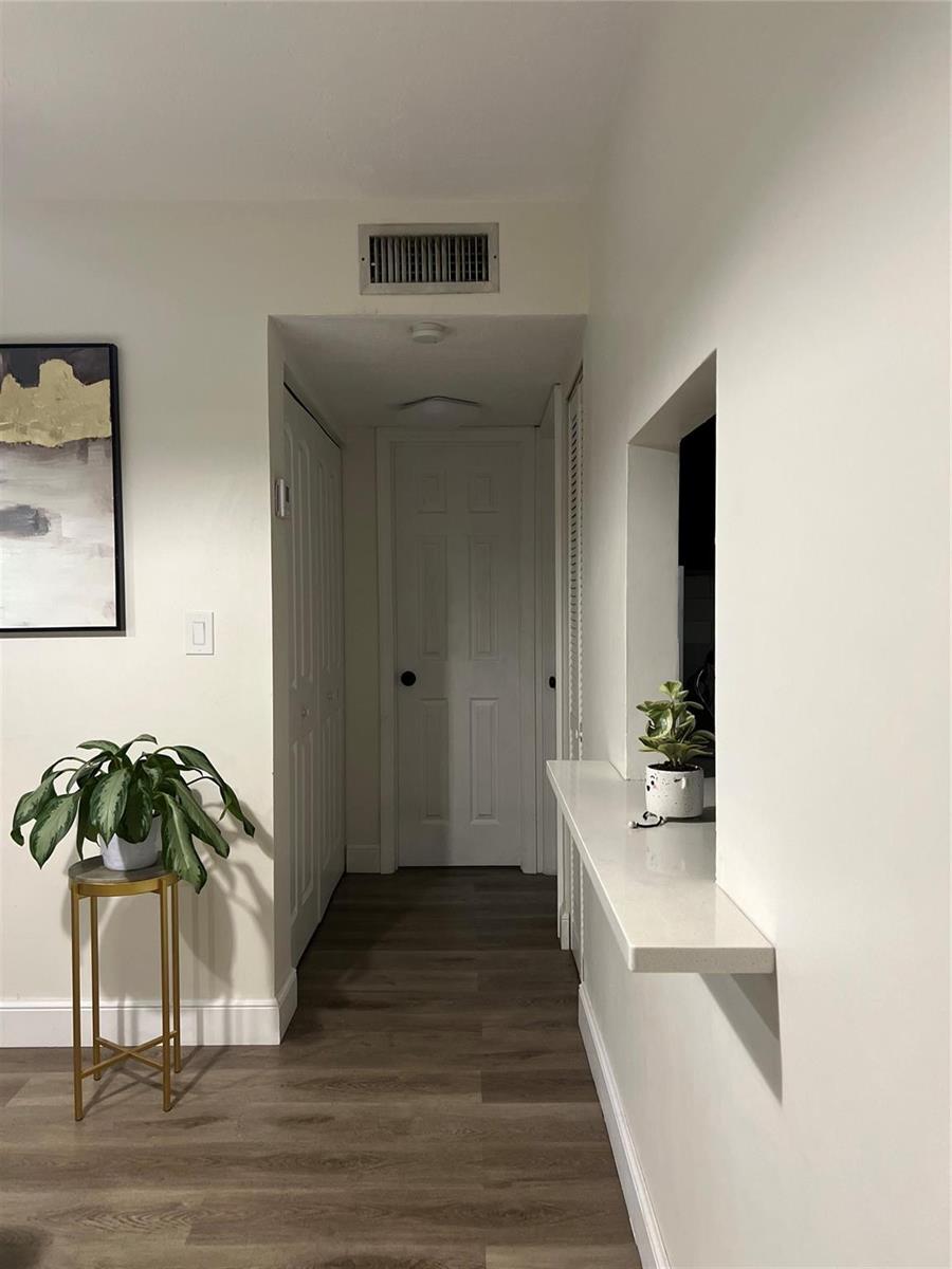 A hallway with wood-look flooring leads to a closed door, featuring a wall-mounted counter — 1061 NW 45th Street # 8, Pompano Beach FL 33064, POMPANO BEACH, FL