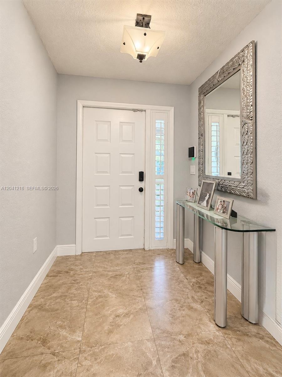 An entryway features light-colored tile flooring, a white front door, and a glass console table — 12224 NW 30th Mnr, Sunrise FL 33323, SUNRISE, FL