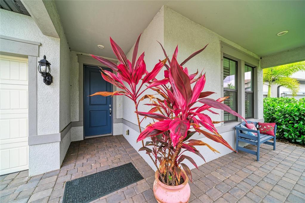 A covered entryway features a blue front door, a potted red plant, and a bench — 16341 HIDDEN OAK LOOP, LAKEWOOD RANCH, FL