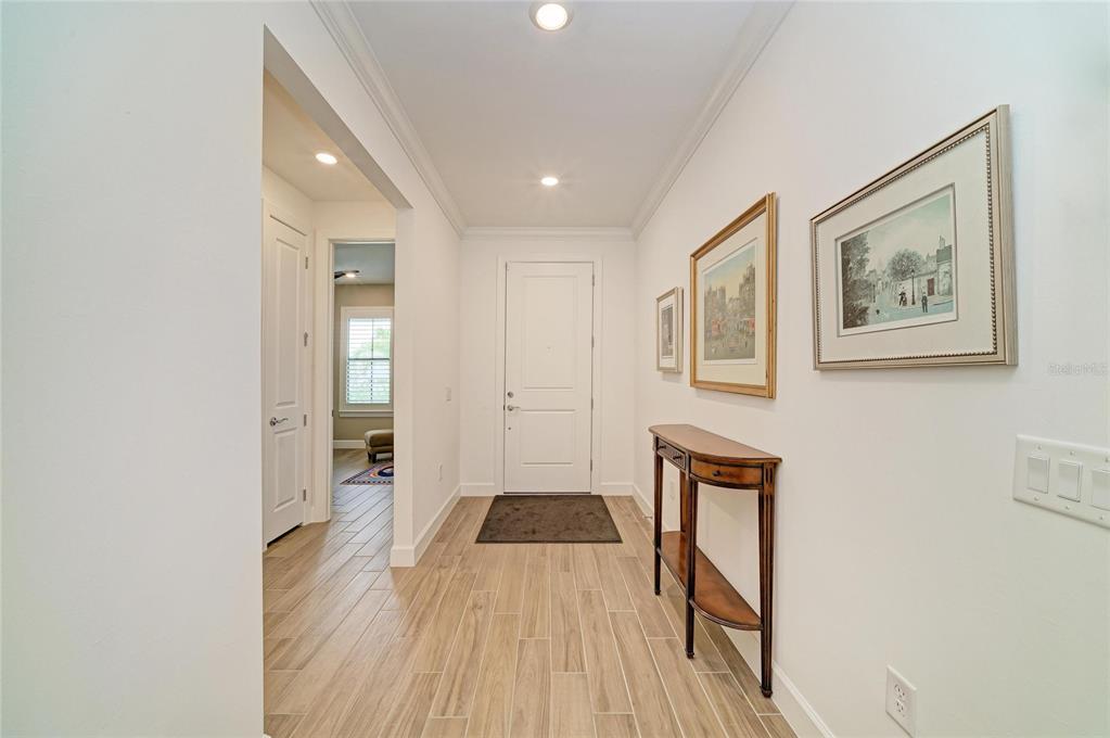 A bright entryway features light wood-look tile flooring, a white door, and a console table — 16341 HIDDEN OAK LOOP, LAKEWOOD RANCH, FL