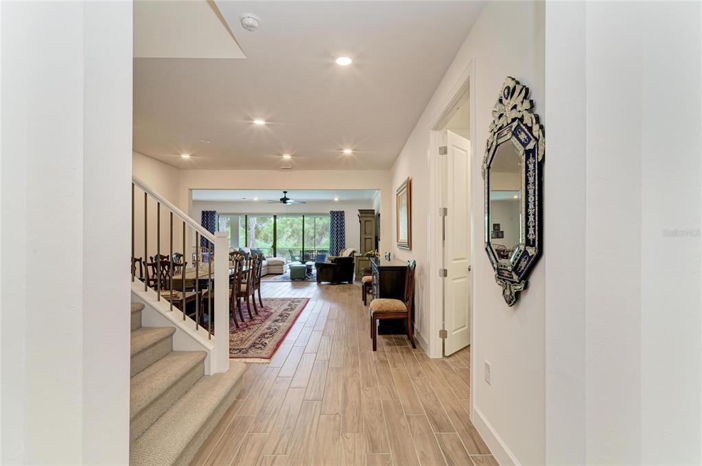 A hallway with wood-look tile flooring leads to a dining area and living space — 16341 HIDDEN OAK LOOP, LAKEWOOD RANCH, FL