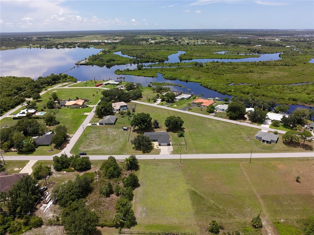 An aerial view shows a residential neighborhood with houses, large grassy lots, and a nearby lake — 31092 N BEND STREET, PUNTA GORDA, FL