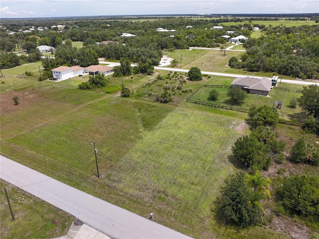 An aerial view shows a vacant, grassy residential lot bordered by a road and trees — 31092 N BEND STREET, PUNTA GORDA, FL
