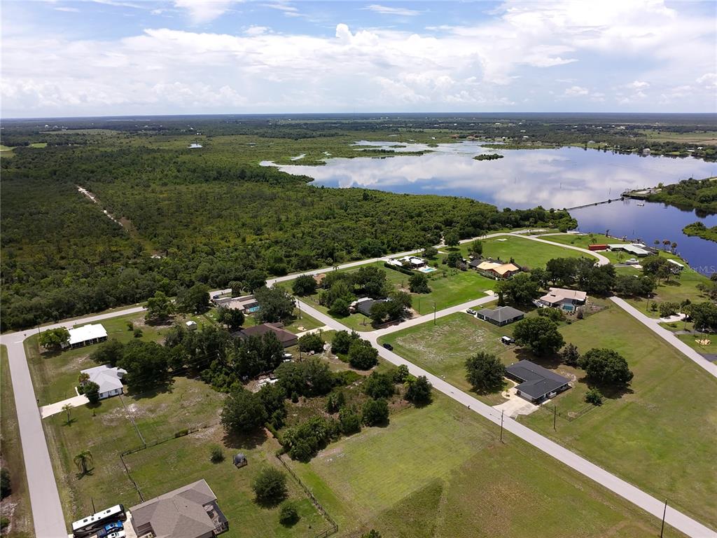 An aerial view shows houses scattered among trees and grassy lots near a large lake — 31092 N BEND STREET, PUNTA GORDA, FL