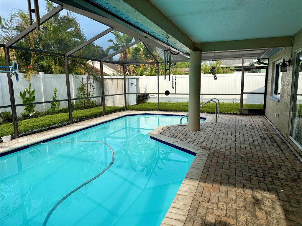A screened-in patio features a swimming pool, brick pavers, and a white vinyl privacy fence — 3670 LAKE BOULEVARD, CLEARWATER, FL