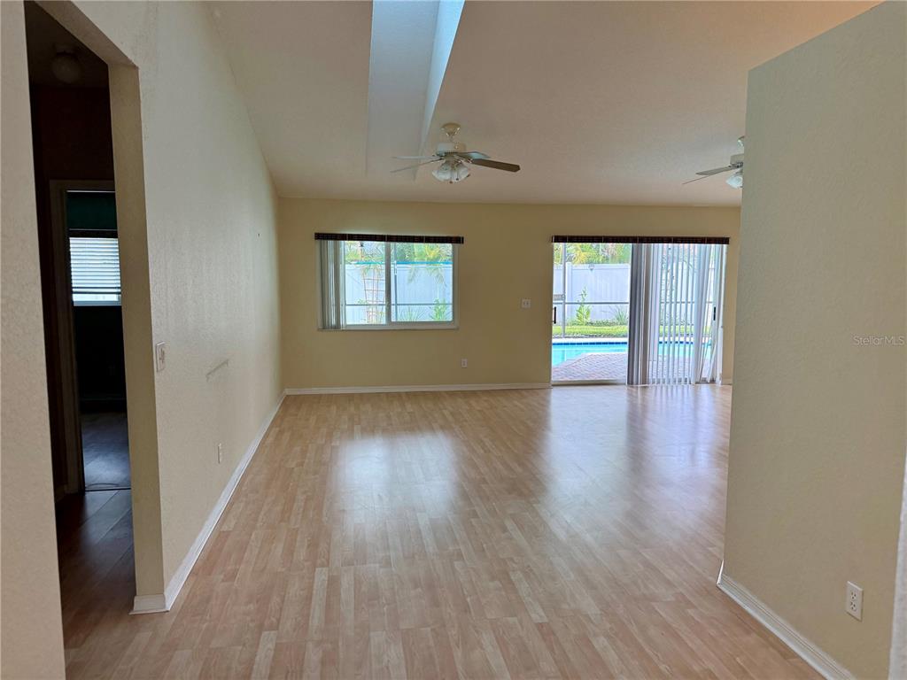 An empty living room features light wood-look flooring, a vaulted ceiling, and sliding glass doors — 3670 LAKE BOULEVARD, CLEARWATER, FL