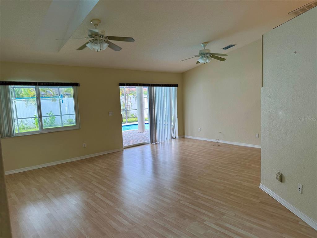 An empty living room features light wood-look flooring, two ceiling fans, and sliding glass doors — 3670 LAKE BOULEVARD, CLEARWATER, FL