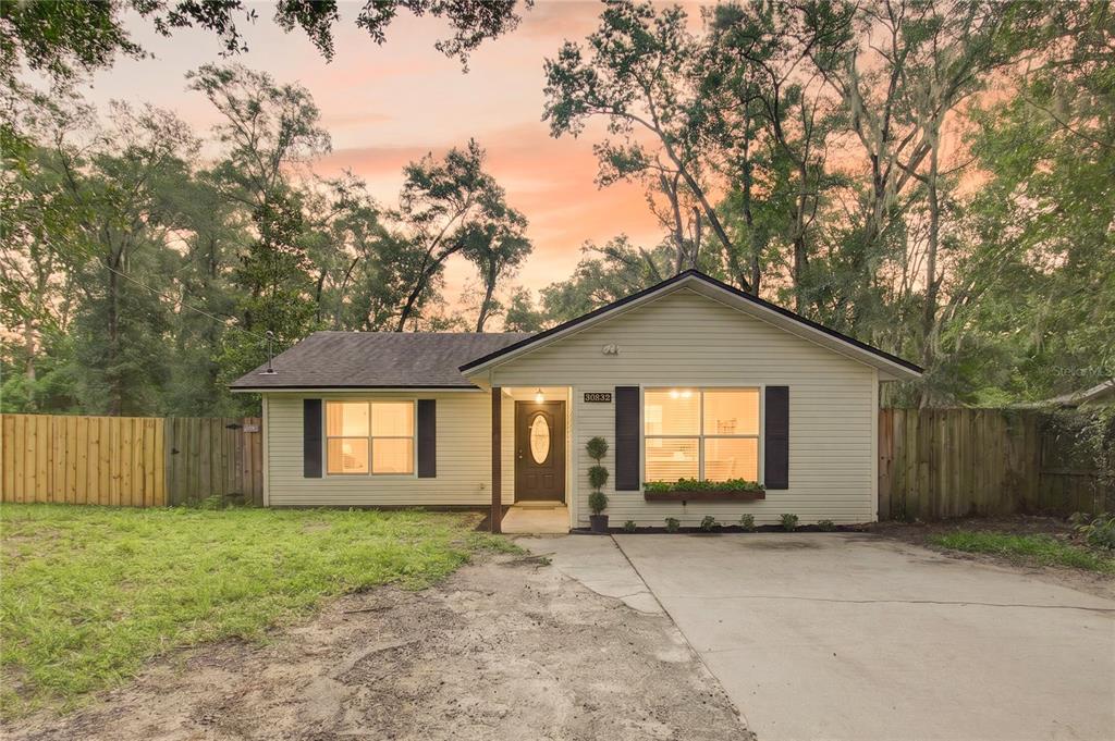 A single-story house with light siding, black shutters, and a concrete driveway under mature trees — 30832 RIDGEVIEW AVENUE, MOUNT PLYMOUTH, FL