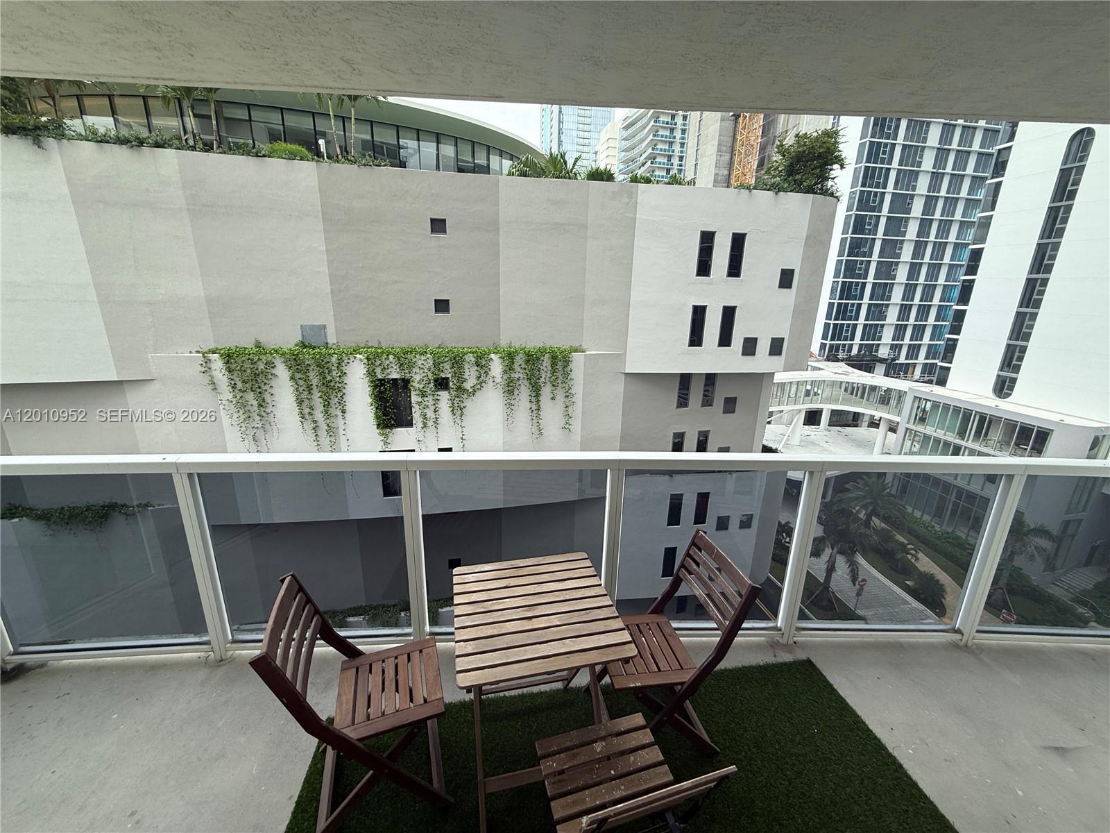 A balcony features a small wooden table and chairs set on a patch of artificial grass — 601 NE 23rd St # 901, Miami FL 33137, MIAMI, FL