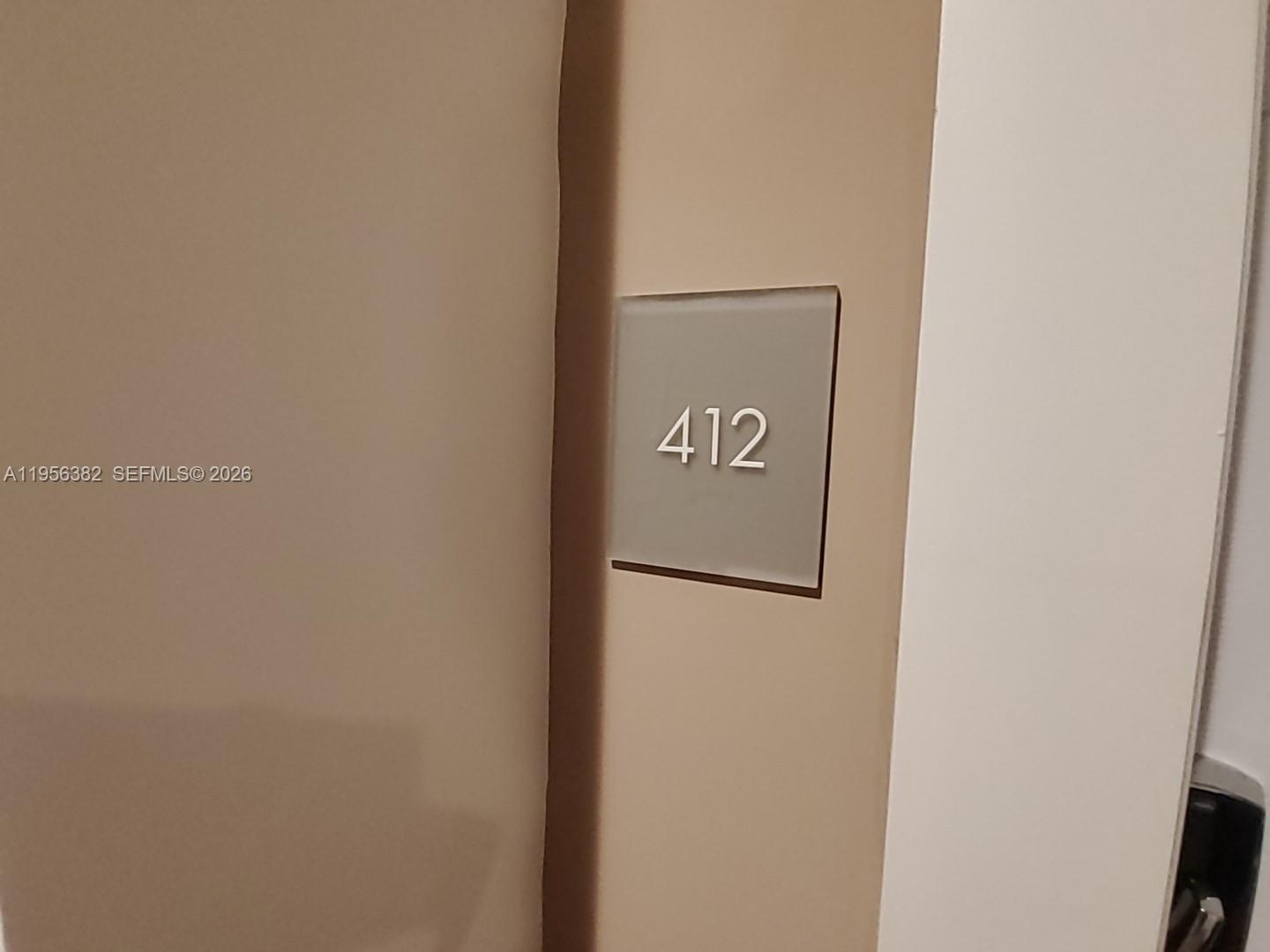 A square, frosted glass sign with the number 412 is mounted on a beige wall — 2000 Metropica Way # 412, Sunrise FL 33323, SUNRISE, FL