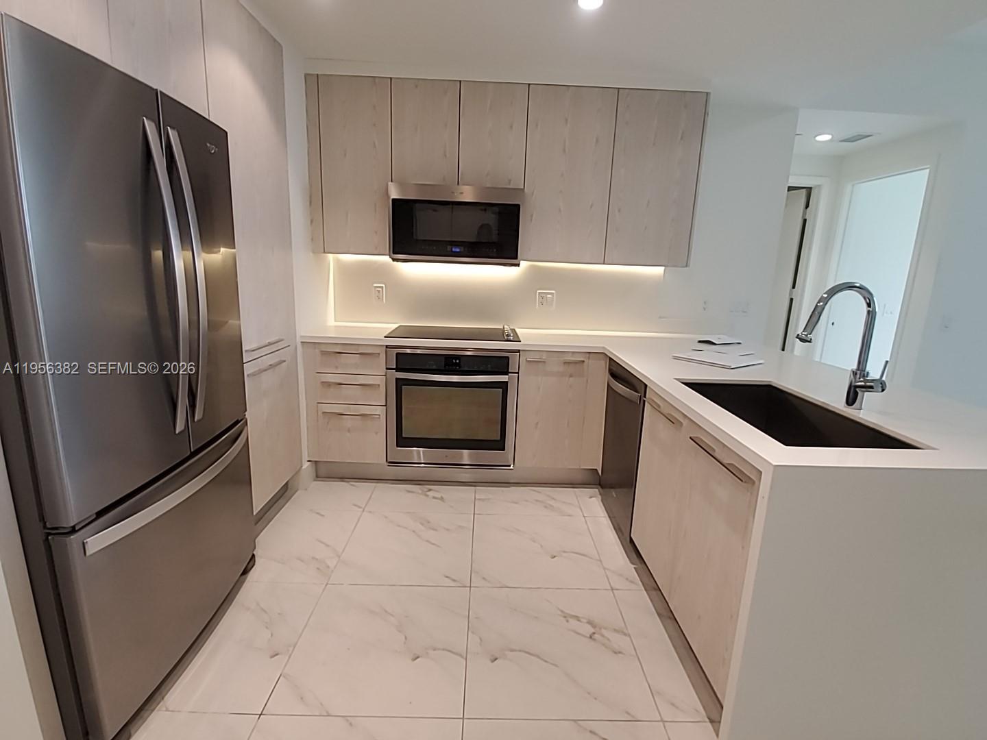A modern kitchen features light wood cabinets, stainless steel appliances, and white marble-patterned tile floors — 2000 Metropica Way # 412, Sunrise FL 33323, SUNRISE, FL