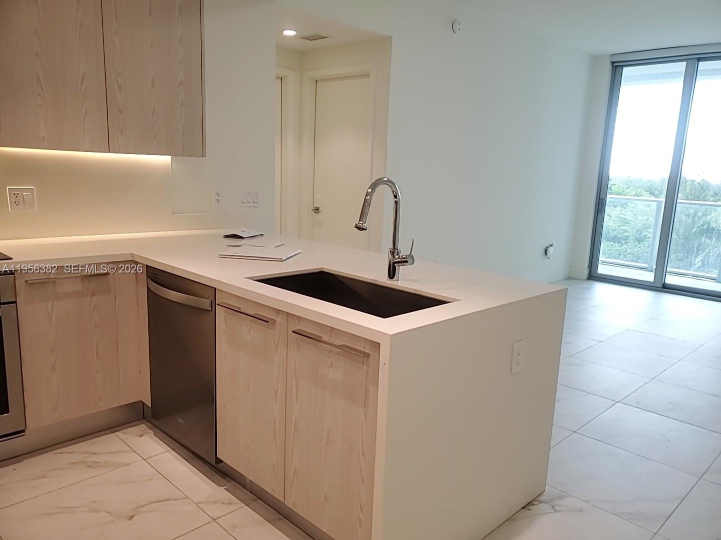 A modern kitchen features light wood cabinets, white countertops, a stainless steel sink, and tile flooring — 2000 Metropica Way # 412, Sunrise FL 33323, SUNRISE, FL