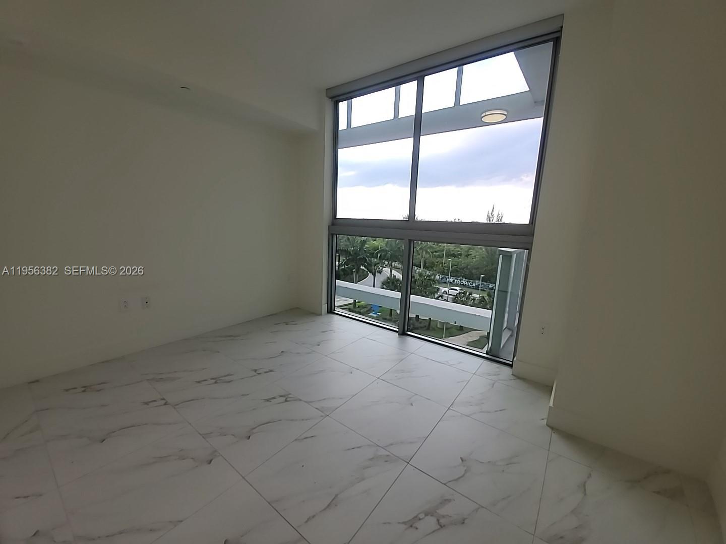 An empty room features white marble-look tile floors and a large floor-to-ceiling window — 2000 Metropica Way # 412, Sunrise FL 33323, SUNRISE, FL