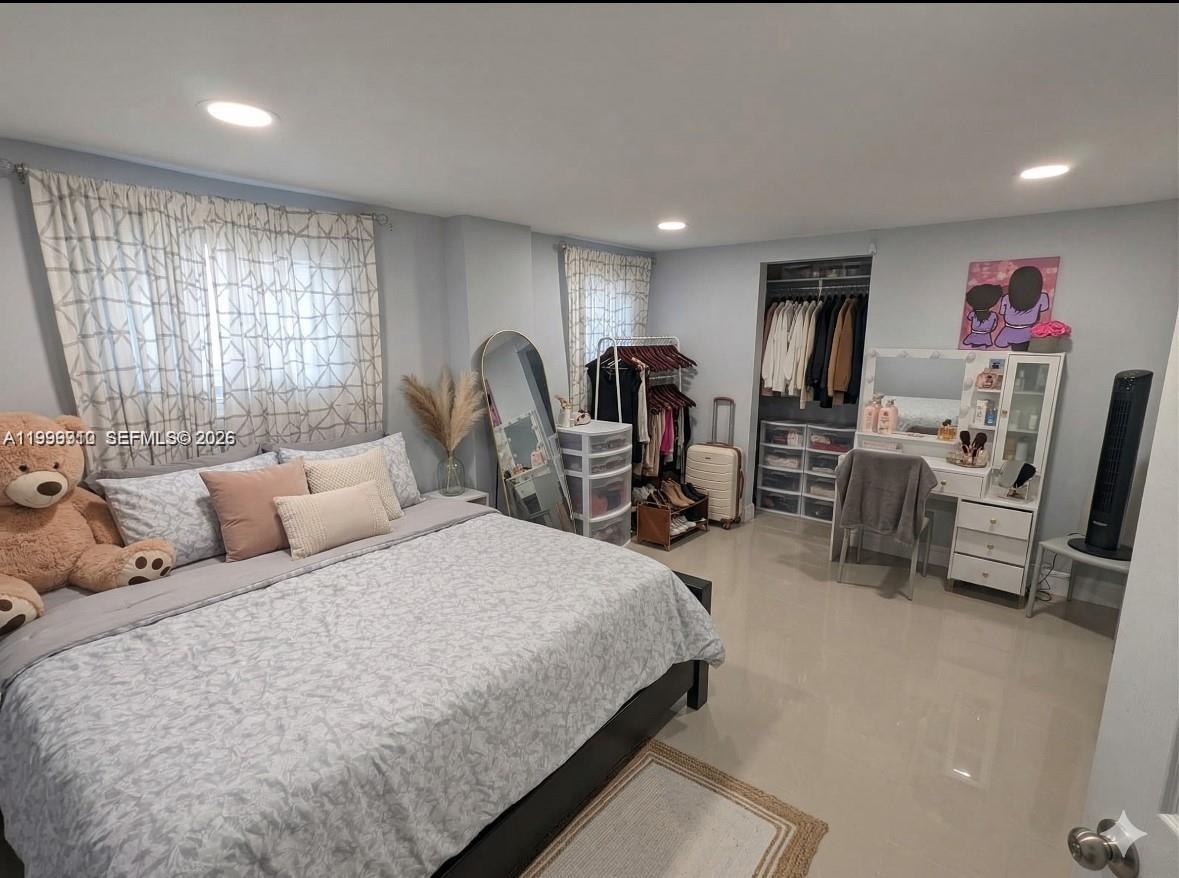 A bedroom with light blue walls, tile flooring, a bed, a vanity, and an open closet — 442 NE 162nd St, Miami FL 33162, MIAMI, FL