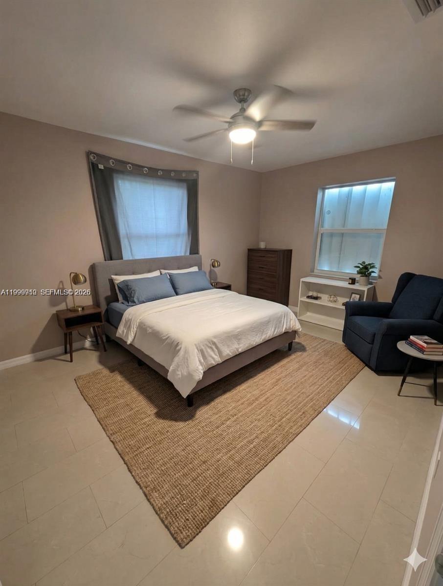 A bedroom features a gray upholstered bed, a blue armchair, and a large area rug — 442 NE 162nd St, Miami FL 33162, MIAMI, FL