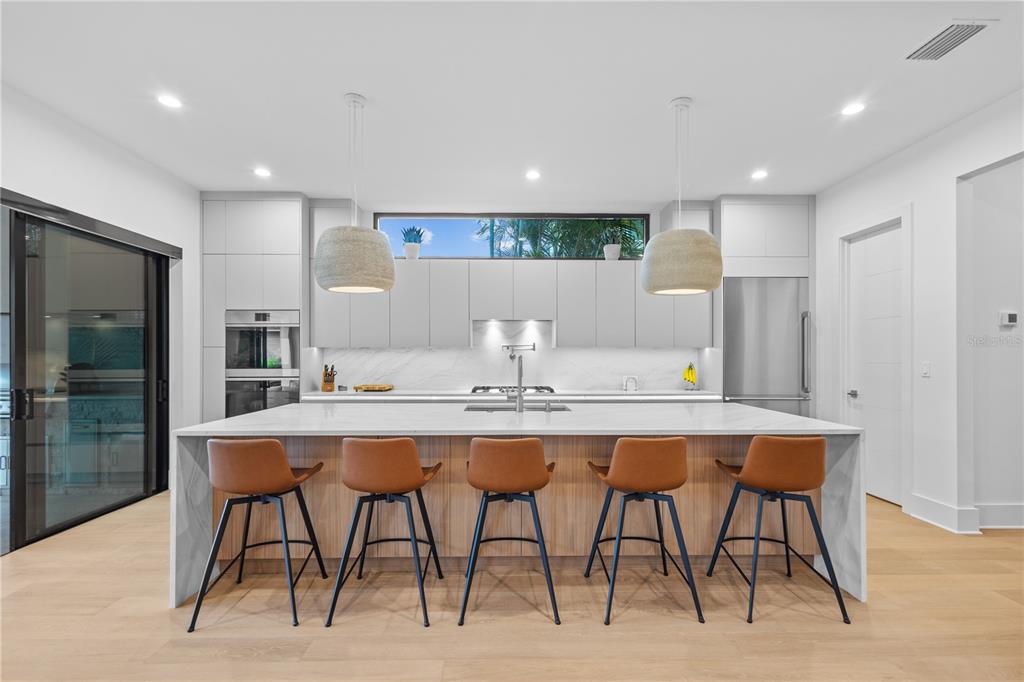A modern kitchen features a large white marble island with five brown stools and cabinetry — 805 W INDIANA AVENUE, TAMPA, FL