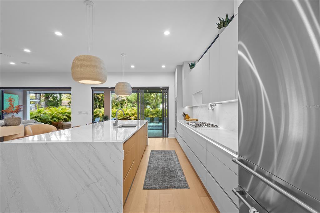 A modern kitchen features a marble waterfall island, light wood cabinetry, and stainless steel appliances — 805 W INDIANA AVENUE, TAMPA, FL