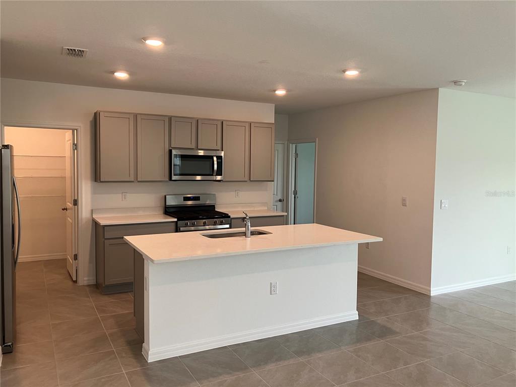 A kitchen features gray cabinets, a white island with a sink, and stainless steel appliances — 35694 KINSEY POINT, ZEPHYRHILLS, FL