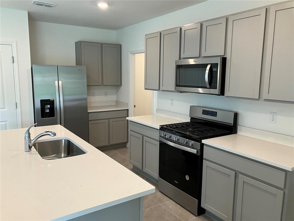A kitchen featuring gray cabinets, stainless steel appliances, and a white quartz-topped island — 35694 KINSEY POINT, ZEPHYRHILLS, FL