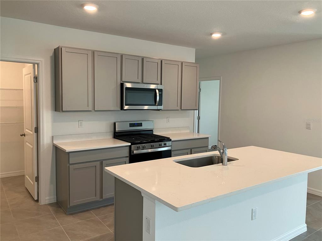 A kitchen features gray cabinets, white countertops, a center island with a sink, and appliances — 35694 KINSEY POINT, ZEPHYRHILLS, FL