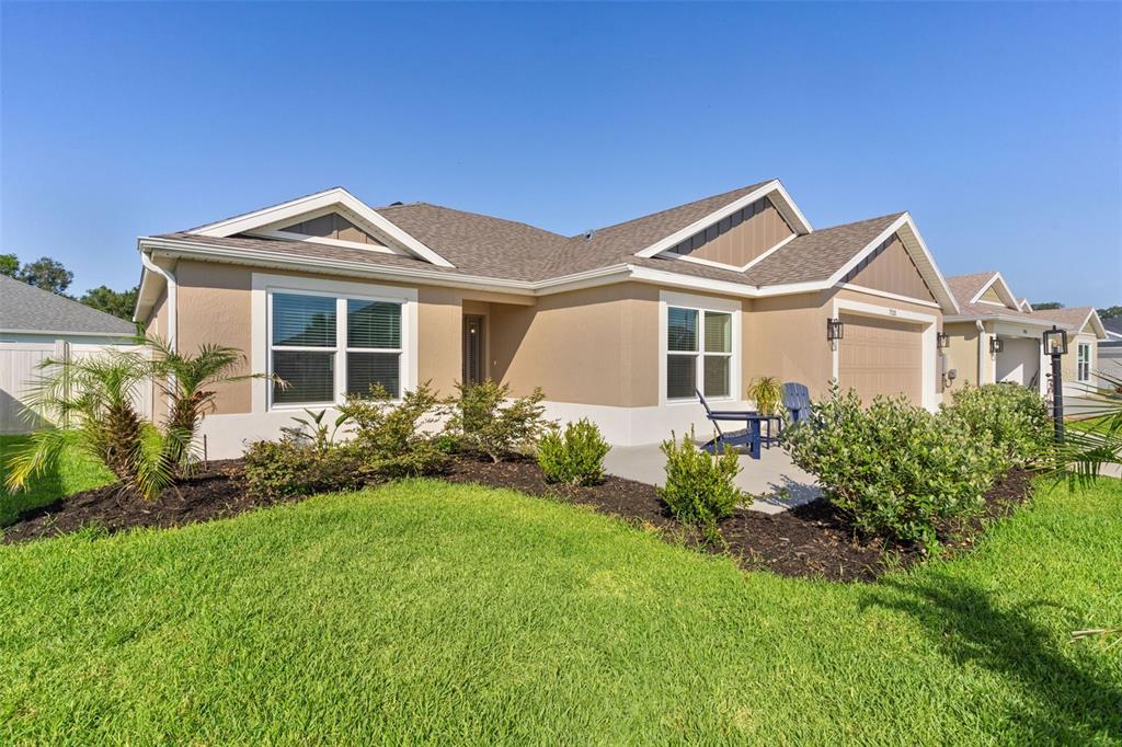 A single-story house with tan stucco walls, a brown shingled roof, and a front lawn — 7520 FAR HILLS LOOP, THE VILLAGES, FL