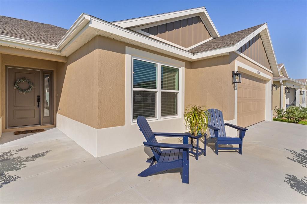 A tan house exterior features a front porch with two blue chairs and a plant — 7520 FAR HILLS LOOP, THE VILLAGES, FL