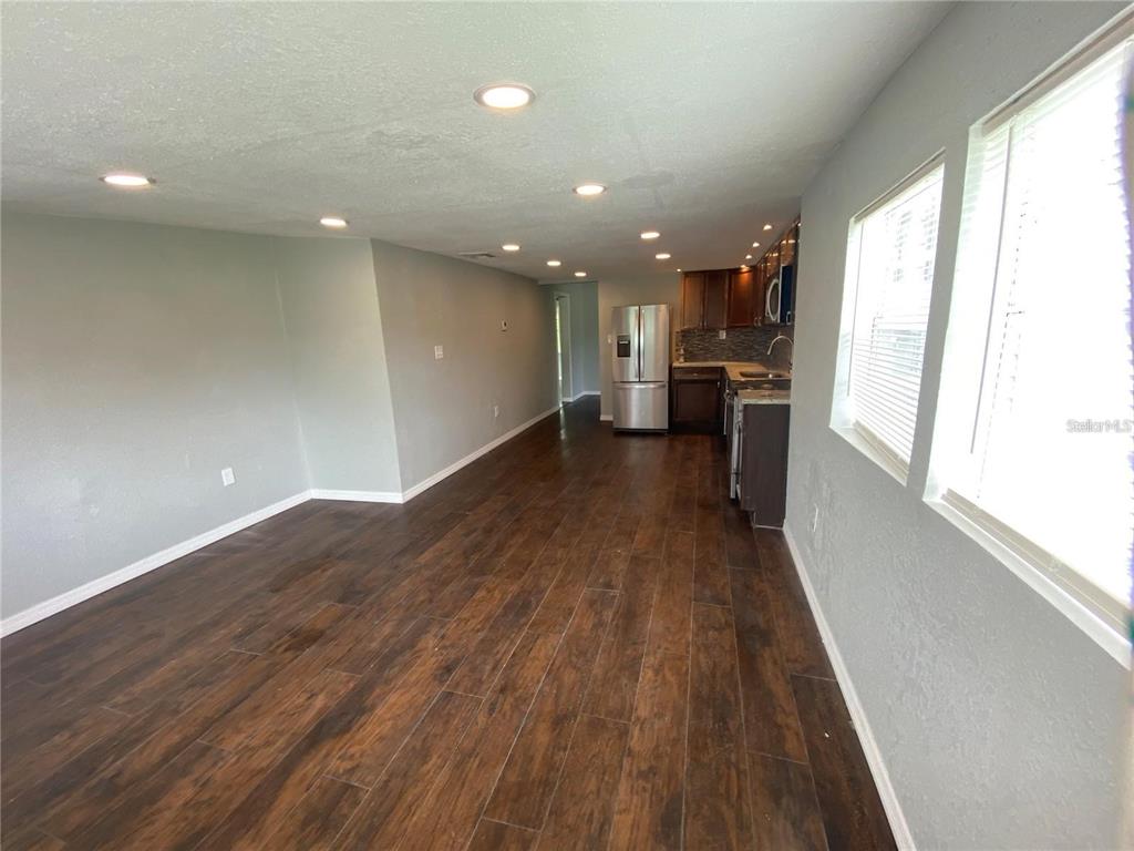 A living room with dark wood-look flooring leads into a kitchen with stainless steel appliances — 306 PALMETTO AVENUE NW, WINTER HAVEN, FL