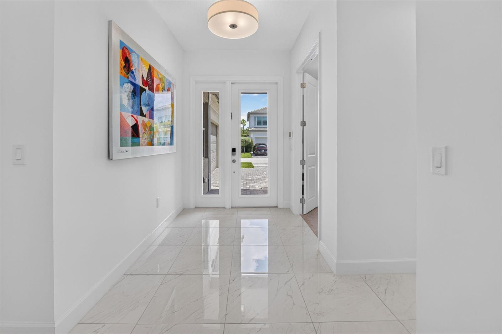 A bright entryway features white walls, marble-look tile flooring, a modern ceiling light, and artwork — 13197 Whistler Mountain Road, Delray Beach FL 33446, DELRAY BEACH, FL