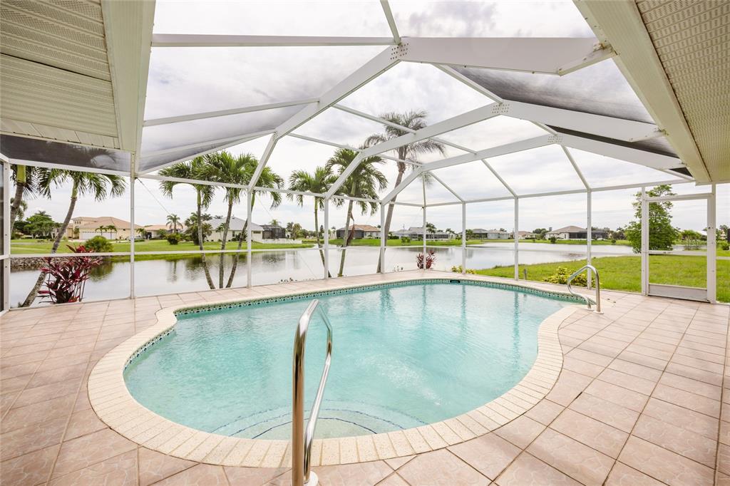 A screened-in patio features a kidney-shaped swimming pool overlooking a lake and palm trees — 24102 SANTA INEZ ROAD, PUNTA GORDA, FL