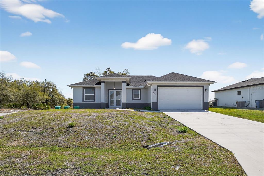 A single-story house with a white garage, gray exterior, and a concrete driveway — 4630 GENE AVENUE N, LEHIGH ACRES, FL