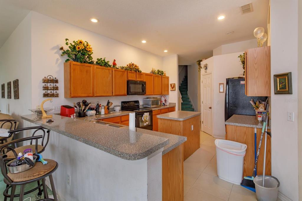 A kitchen features wood cabinets, granite countertops, a breakfast bar, and a black refrigerator — 244 BALLYSHANNON DRIVE, DAVENPORT, FL