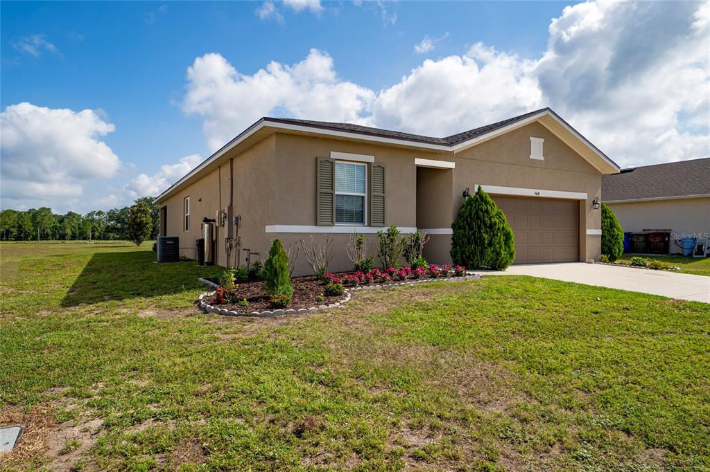 A single-story tan stucco house with a two-car garage and a landscaped front garden — 5610 WESTERN SUN DRIVE, ST CLOUD, FL